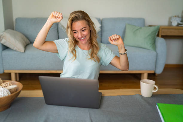 istock Woman with raised hands looking at laptop while sitting at home 1869766970