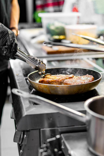 istock Professional chef cooking beef steak in frying pan on stove in restaurant kitchen 1869788638