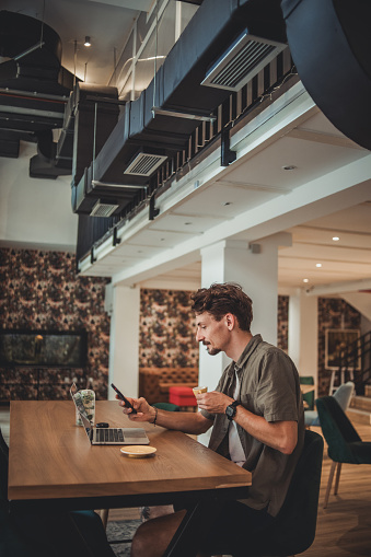 A young hipster man in a cafe drinking coffee and using a mobile phone to surf the Internet or correspond on social networks