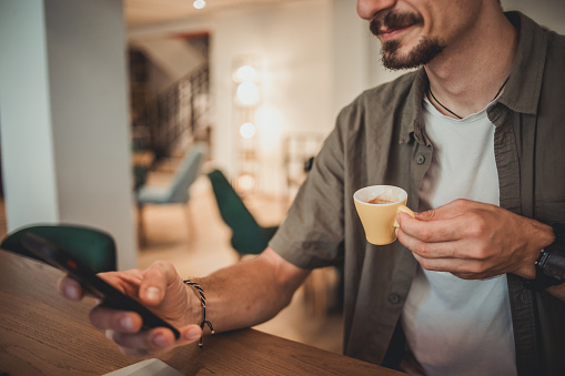 A young hipster man in a cafe drinking coffee and using a mobile phone to surf the Internet or correspond on social networks