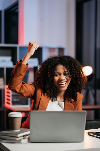 Overjoyed charming excited black woman business woman worker using smartphone and laptop working in office, feeling happy.