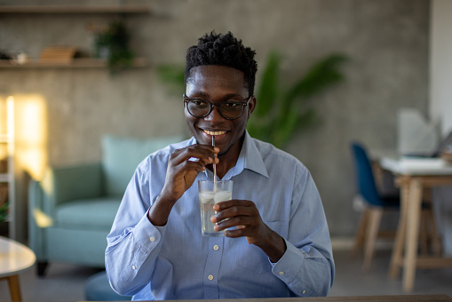 A young African American man drinking cold juice with a metal straw in his apartment