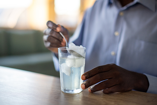 A young African American man removing ice from a drinking glass using a spoon in his apartment