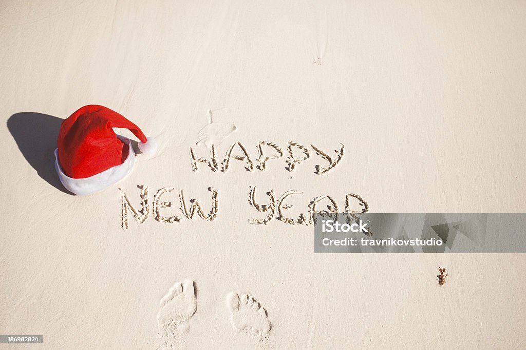 Happy New Year written in the sand and Santa Hat Happy New Year written in the sand and Santa Hat on white sandy beach Beach Stock Photo