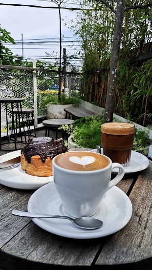 An outdoor cafe view with having a hot flat white coffee, a glass of long black coffee, and an ovomaltine danish bread.