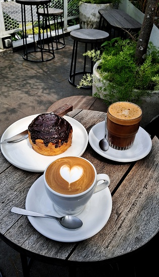 A high angle view of a heart-shaped coffee, a foamy coffee, and a coco bread on the wooden table.