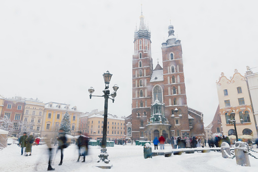 Long Exposure of heavy snowfall over the mai square of the Old Town and authentic buildings decorating by Christmas decorations with crowds of people walking in Krakow, Poland, Europe