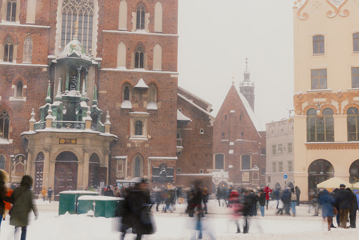 Long Exposure of heavy snowfall over the mai square of the Old Town and authentic buildings decorating by Christmas decorations with crowds of people walking in Krakow, Poland, Europe