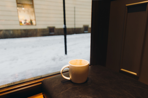 View of cup with coffee with window view of snow falling the old streets
