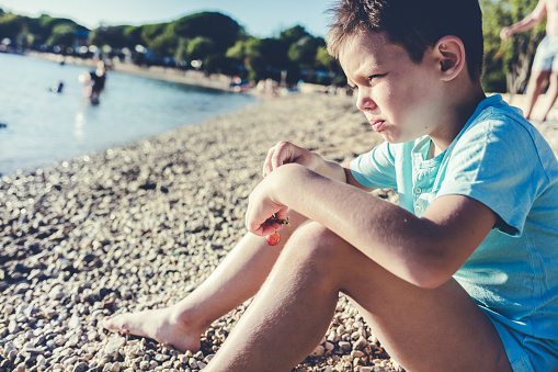 Little boy sitting in sand on the beach and enjoying in summer day. Copy space.
