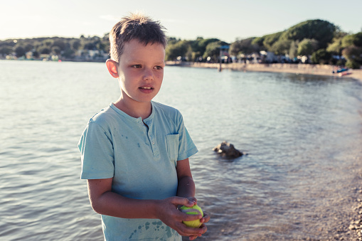 Teenage boy playing with ball on the city beach. Happy cute little boy playing with ball in sea.