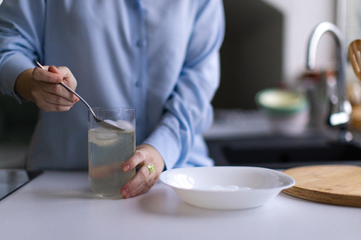 A young Caucasian woman removing ice from a drinking glass using a spoon in the kitchen of her apartment