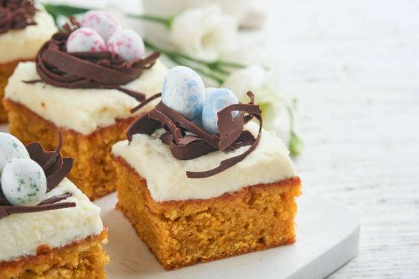 istock Easter carrot cake bars decorated with chocolate nest and chocolate candy eggs blossoming cherry or apple flowers on rustic light wooden backgrounds. Easter holiday meal. Traditional Easter food. 1869902374