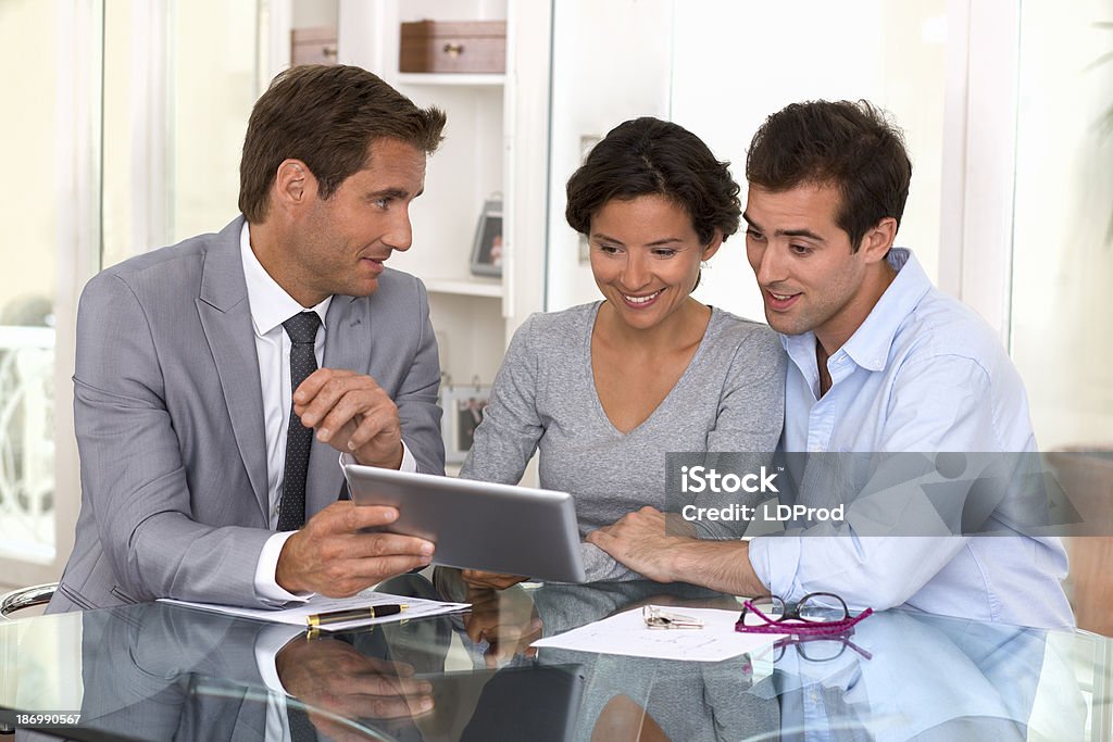 Architect presenting new project to a smiling young couple tablet pc woman man businessman indoor contract Couple - Relationship Stock Photo