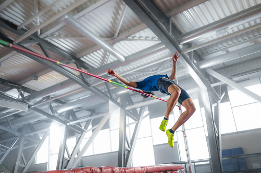 Young athlete doing high jump in sports hall during practice.