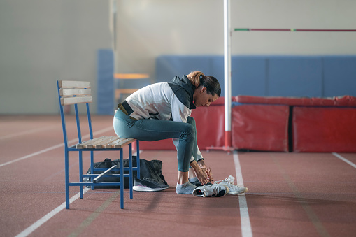 Athlete  young woman putting shoe while sitting in sports hall.