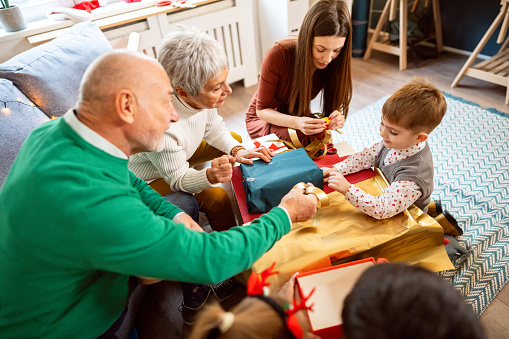 Caucasian toddler boy with multi-generation family wrapping Christmas and New Year presents