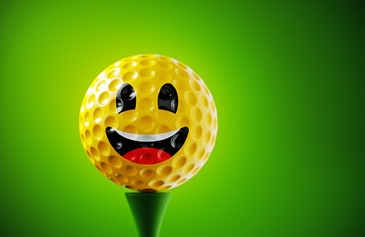 Smiley face printed yellow golf ball on green background. Horizontal composition.
