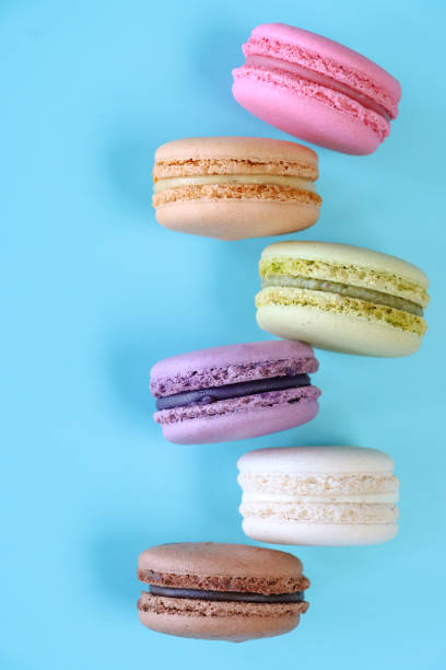 istock Close-up image of staggered column of six macarons, multi coloured macarons filled with flavoured butter cream, chocolate, vanilla, blueberry, pistachio, orange, strawberry flavoured meringues, blue background, elevated view 1869937935