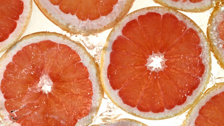 Super slow motion of grapefruit slices with water splashing.