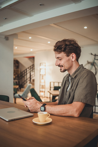 A young hipster man in a cafe drinking coffee and using a mobile phone to surf the Internet or correspond on social networks