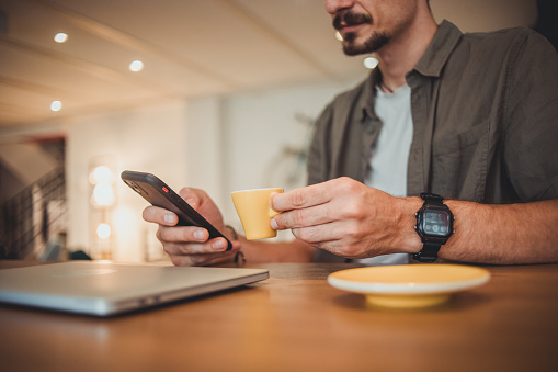 A young hipster man in a cafe drinking coffee and using a mobile phone to surf the Internet or correspond on social networks