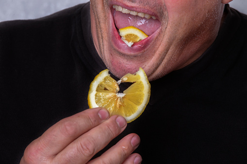 An unrecognizable man eats a sour lemon.