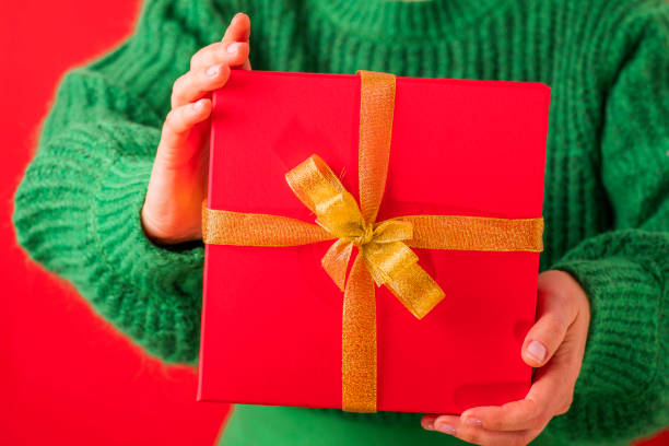 istock Festive Elegance: A Red Gift Box Tied in Gold, Held by Green Comfort 1869956975