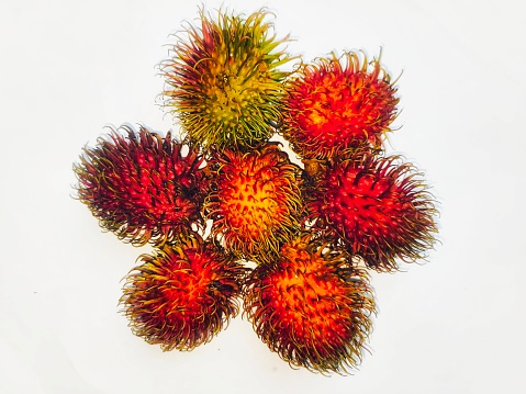 Fresh Thai Rambutans on an old white wooden table, with one cut open showing the delicious fruit inside the hairy skin. 