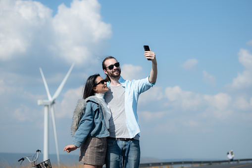 happy young couple taking selfie with smartphone in front of windmills