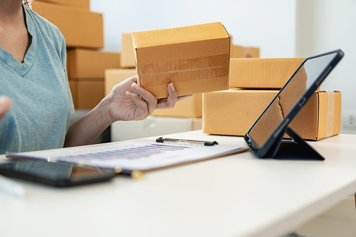 Asian woman working from home SME entrepreneurs use smartphones and laptops for commercial monitoring. Online marketing packed in a parcel box. Close-up image