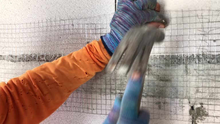 Construction workers are hammering nails into the steel grid before plastering the lightweight brick wall.