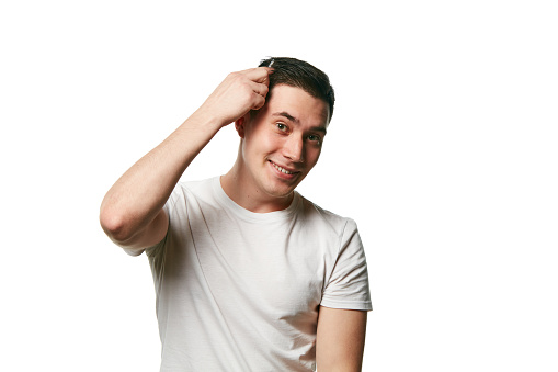 Portrait of attractive young man looks at camera and smile while combing his hair against white background. Concept of beauty treatment and hygiene, body care, hair care, hairstyle, barber.