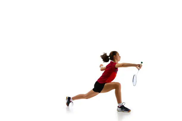 Photo of Dynamic portrait capturing athleticism of young, attractive female badminton player in motion during training against pristine white background.