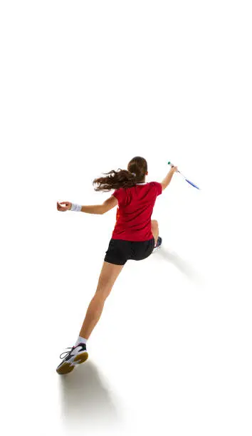 Photo of Dynamic portrait of fit and attractive young woman showcasing her badminton skills in action, epitomizing attack and defense against white background.