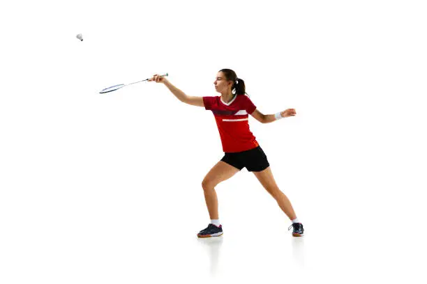 Photo of Full length portrait of badminton athlete demonstrates her skills in attack and defense against white studio background.