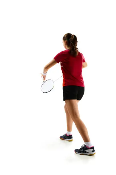 Photo of Rear view portrait of young girl, skilled badminton player practicing with intensity against pristine white background. Concept of sport.