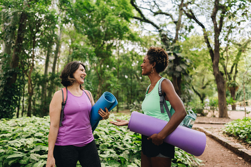 Friends holding exercise mats talking on the public park