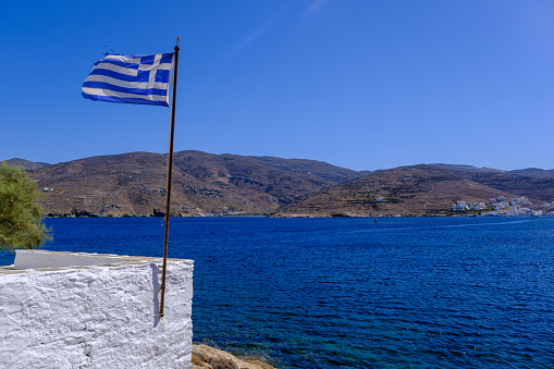 Greek flag waving over blue sky and sea on Tinos Island