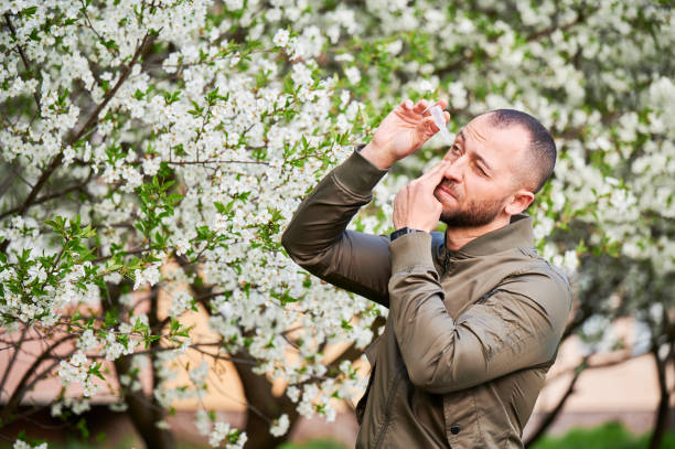 istock Man allergic using medical eye drop, suffering from seasonal allergy at spring in blossoming garden 1870048429