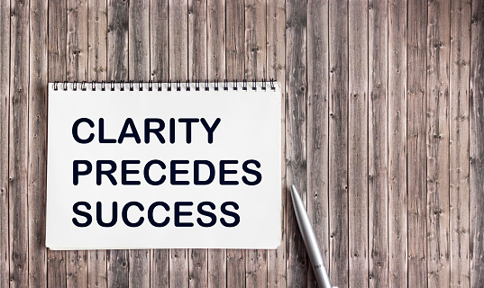 Clarity precedes success concept written on a notepad isolated on a wooden table.