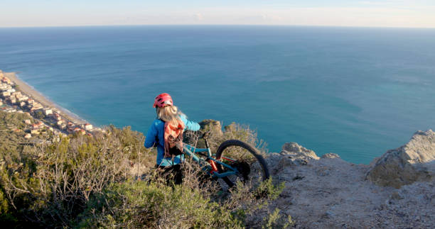 Young woman mountain biker on cliff Young woman mountain biker carries bike down cliff above sea top view on people walking and cyclists riding stock pictures, royalty-free photos & images