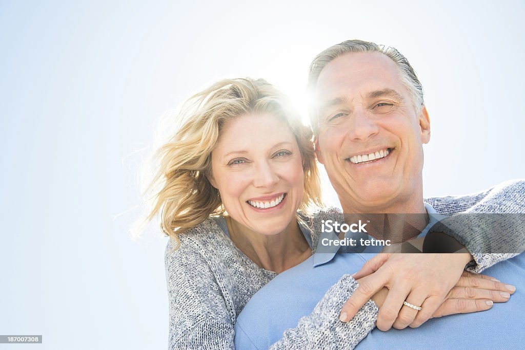 Cheerful Woman Embracing Man From Behind Against Sky Low angle portrait of cheerful mature woman embracing man from behind against clear sky Mature Couple Stock Photo