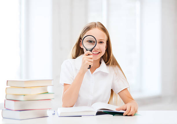 istock girl reading book with magnifier at school 187007614
