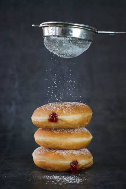 Stock photo showing close-up view of a batch of three stacked, raspberry jelly doughnuts. The doughnuts have been fried, injected with a generous amount of jam and then coated in powdered sugar.