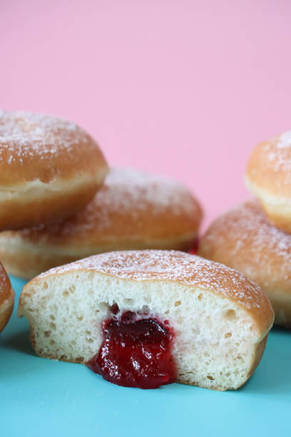 istock Image of fresh jam doughnuts coated in icing sugar, raspberry jam oozing from cut jelly cake half, pink and turquoise split background, focus on foreground 1870098602
