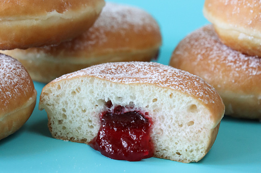 Stock photo showing close-up view of a batch of raspberry jelly doughnuts. The doughnuts have been fried, injected with a generous amount of jam and then coated in caster sugar.