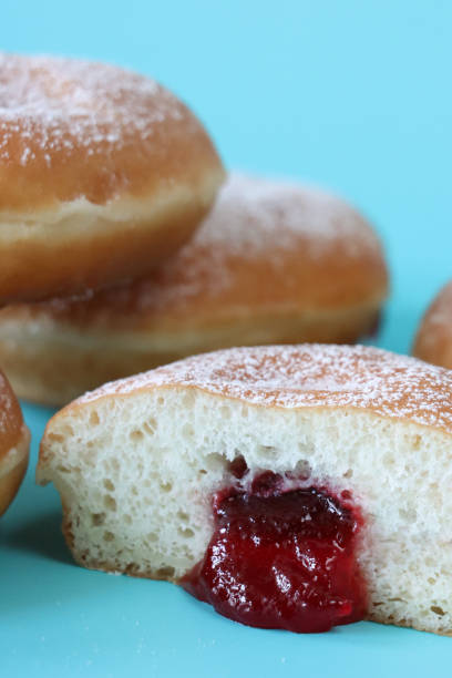 istock Close-up image of fresh jam doughnuts coated in icing sugar, raspberry jam oozing from cut jelly cake half, turquoise background, focus on foreground 1870098604