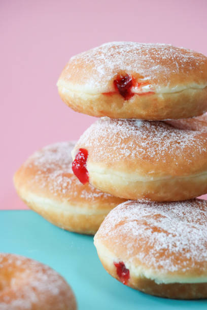 istock Image of stack of fresh jam doughnuts coated in icing sugar, raspberry jam dripping from injection hole, jelly cake half, pink and turquoise split background, focus on foreground 1870098605