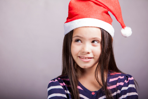 Studio shot of a cute Latin little girl wearing a Santa's hat and looking towards copy space